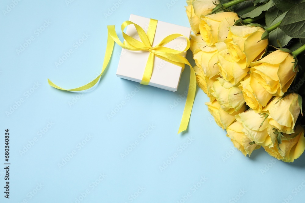 Sticker Beautiful bouquet of yellow roses and gift box on light blue background, flat lay. Space for text