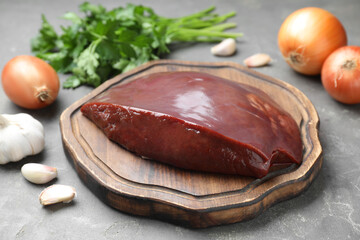 Piece of raw beef liver and products on grey table, closeup