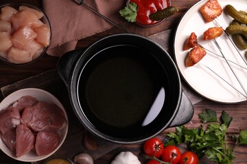 Fondue pot, forks with fried meat pieces and other products on wooden table, flat lay