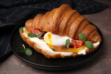Tasty croissant with fried egg, tomato and microgreens on brown textured table, closeup