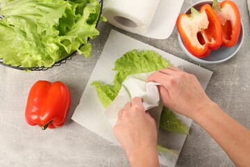 Woman wiping lettuce with paper towels at grey table, top view