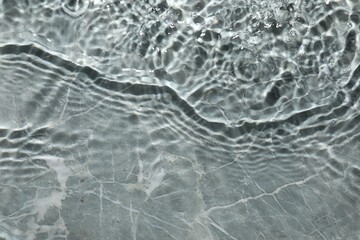 Rippled surface of clear water on light grey textured background, top view