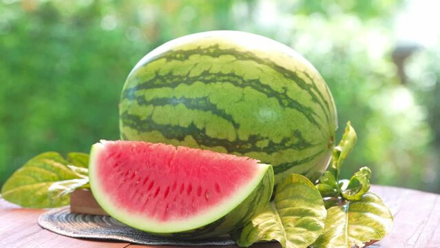 Giant Seedless Watermelon in wooden basket on wooden table in garden, Fresh Watermelon with slices on blurred greenery background.