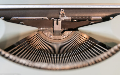 Close-up detail of a vintage typewriter with shallow depth of field. The typewriter is mint green, and its key hammers and ribbon are clearly visible.
