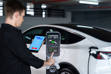 Young man travel with EV electric car to shopping center parking lot charging in downtown city...
