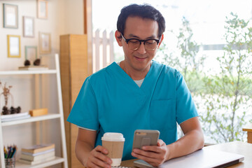 Smiling nurse using digital tablet in employee lounge. Male nurse takes a break outside of a coffee...