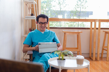 Fototapeta na wymiar Smiling nurse using digital tablet in employee lounge. Happy nurse resting on couch in lounge area and drinking cup of coffee.