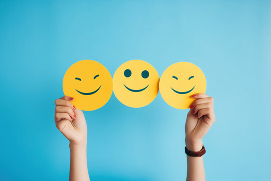 Hands holding smiley emoticons isolated on blue
