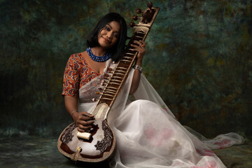 a woman wearing white saree and blue necklace holding harp/veena in hand and handbag promoting peace and harmony 