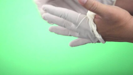 A close-up shot of a woman's hands taking off white latex gloves and hanging them together on a green screen background