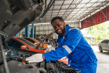 Fototapeta na wymiar Mechanic working under the hood at the repair garage. Portrait of a happy mechanic man working on a car in an auto repair shop. Male mechanic working on car.