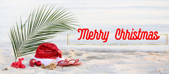 Greeting banner for Merry Christmas and Happy New Year with Santa hat, decor, tropical leaf and flip-flops on beach sand © Pixel-Shot