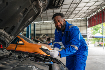 Fototapeta na wymiar Mechanic working under the hood at the repair garage. Portrait of a happy mechanic man working on a car in an auto repair shop. Male mechanic working on car.
