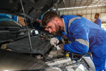 Mechanic working under the hood at the repair garage. Portrait of a happy mechanic man working on a car in an auto repair shop. Male mechanic working on car.
