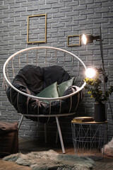 Stylish armchair and glowing lamps on table near grey brick wall