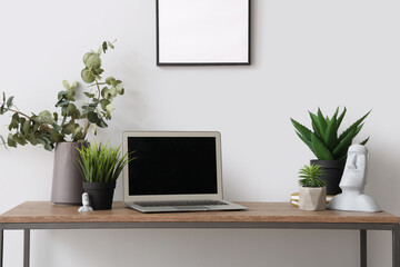 Modern laptop and different houseplants on table near white wall