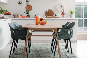 Wooden dining table with orange juice and fresh fruits in modern kitchen