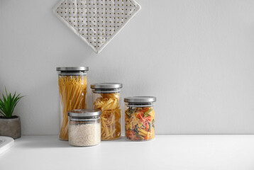 Glass jars with different types of pasta on white counter in kitchen