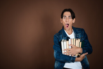 Funny student posing with books in studio on brown background.