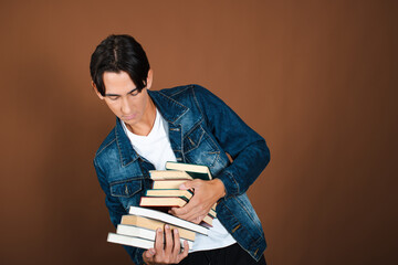 Funny student posing with books in studio on brown background.