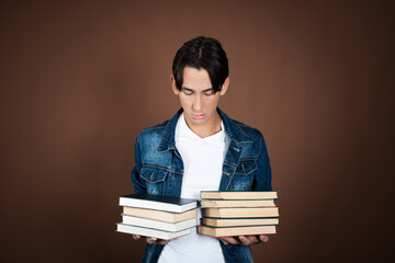 Funny student posing with books in studio on brown background.