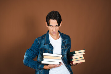 Funny student posing with books in studio on brown background.