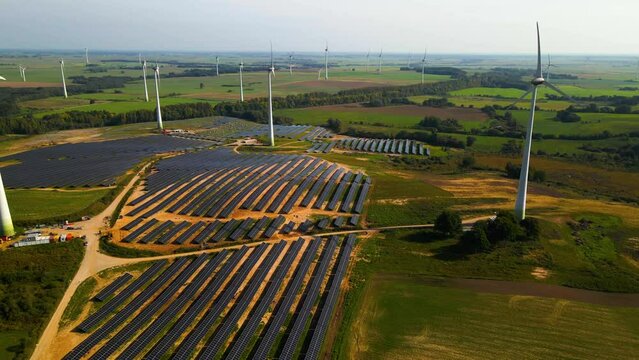 Aerial footage of solar panels plant and wind turbines in a wind farm generating green electric energy on a wide green field on a sunny day, in Taurage, Lithuania, pan right