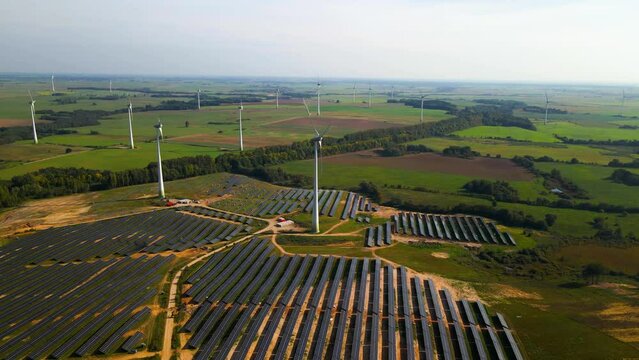 Aerial footage of solar panels plant and wind turbines in a wind farm generating green electric energy on a wide green field on a sunny day, in Taurage, Lithuania, zooming in
