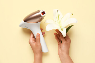 Female hands with modern photoepilator and lily flower on pale yellow background