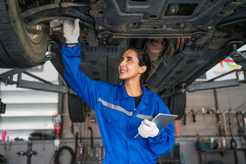 Auto mechanic in blue uniform are repair and maintenance auto engine is problems at car repair shop. Professional Repairman is Wearing Gloves and Using a Ratchet Underneath the Car.