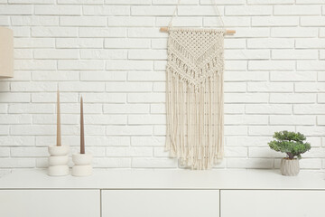 Modern white chest of drawers with candles and houseplant near white brick wall in room