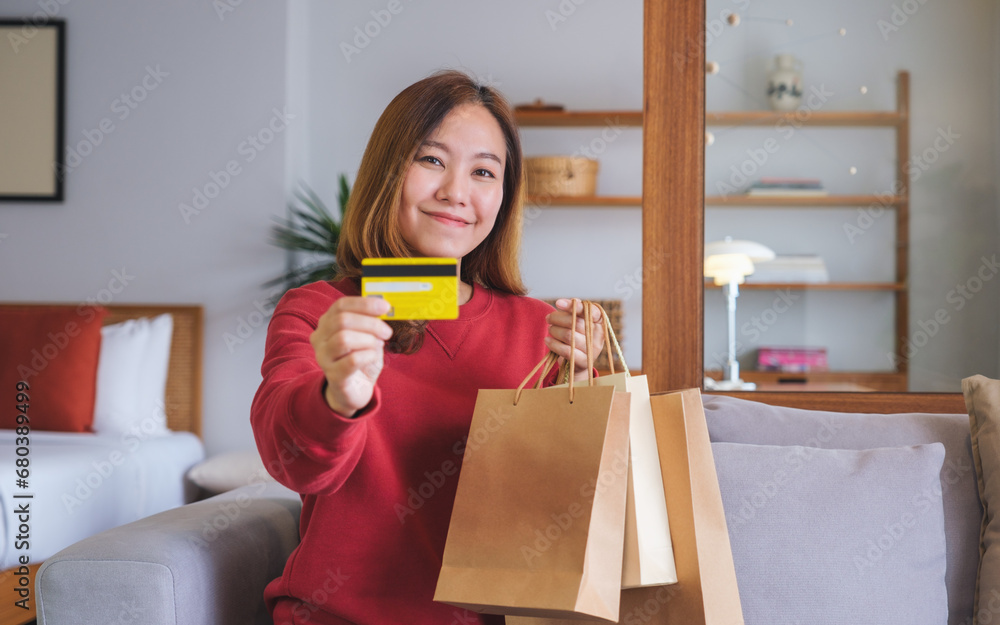 Wall mural Portrait image of a woman with shopping bags holding and showing a credit card for purchasing