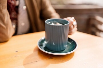 woman holding a cup of hot cappuccino coffee in a cafe on the street, rings on her fingers.