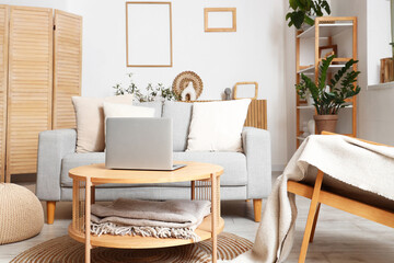 Interior of modern living room with grey sofa and laptop on wooden coffee table