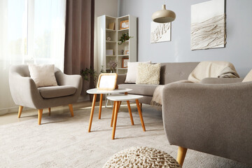 Interior of modern living room with grey sofa, armchairs and blank photo frame on coffee table