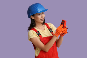 Young female electrician with multimeter and wires on purple background