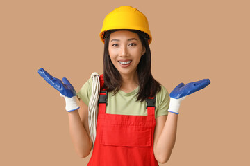 Young female electrician with cables on beige background