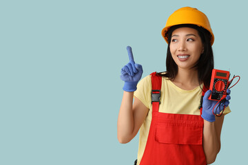 Young female electrician with multimeter pointing at something on blue background