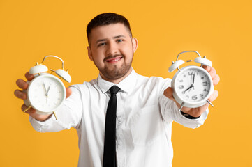 Young happy businessman with alarm clocks on yellow background. Time management concept