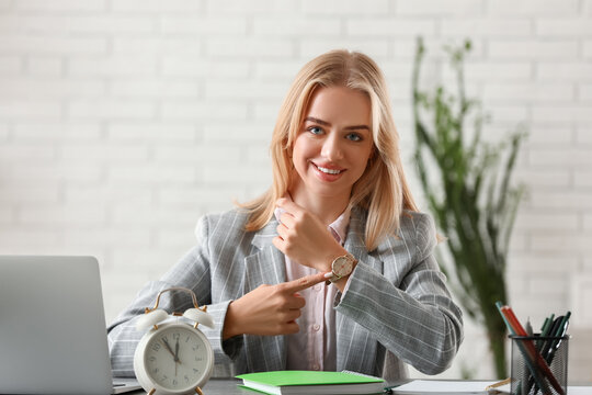 Young happy businesswoman pointing at wrist watch in office. Time management concept