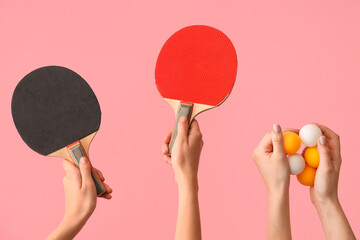 Female hands with ping pong rackets and balls on pink background