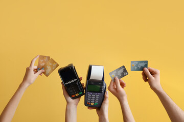 Female hands with payment terminal and credit cards on yellow background
