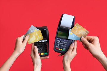 Female hands with payment terminals and credit cards on red background