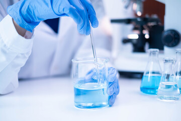 Closeup scientist hand using stirring rod for stirring blue liquid solution glass beaker chemical...