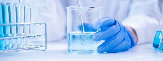 Closeup scientist hand using stirring rod for stirring blue liquid solution glass beaker chemical chemistry research science experiment test laboratory, scientific medicine technology lab analysis