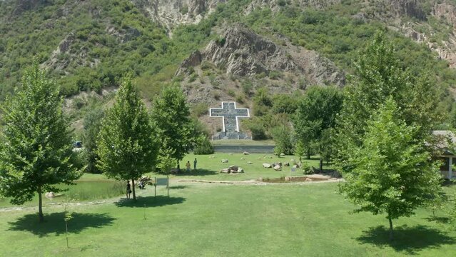 Fly through and a slight tilting drone shot of a cross sculpture built to comemmorate the volcano eruption victims of Kozuh Mountain in the town of Rupite, Petrich, Bulgaria.