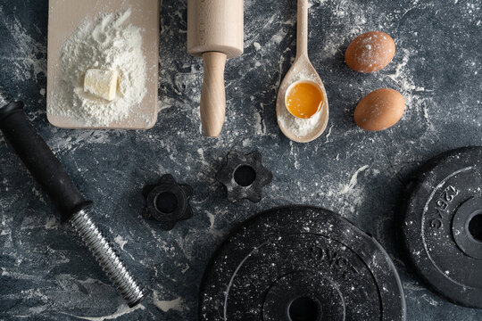 Healthy fitness diet baking flat lay concept. Dumbbell barbell weight plates, kitchen utensils, dough ingredients. Fit nutrition plan food preparation. Gym workout, sport training composition.