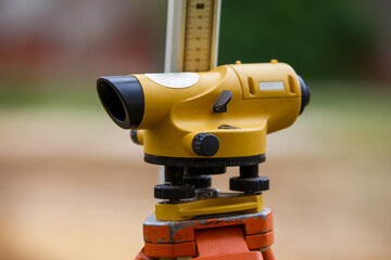 Yellow theodolite on a tripod and a ruler with a blurred background. Geodetic measurements.