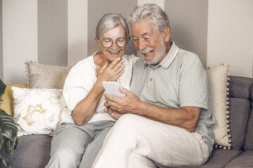 Video call concept. Happy senior couple sitting on sofa video calling by smartphone, old white haired grandparents enjoy technology for online webcam connection with distant family or friends