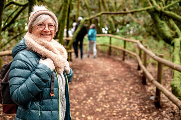 Fototapeta premium Smiling senior woman holding backpack walks in the Garajonay national park in La Gomera. Elderly active woman hiking in mountain forest enjoying nature and healthy lifestyle